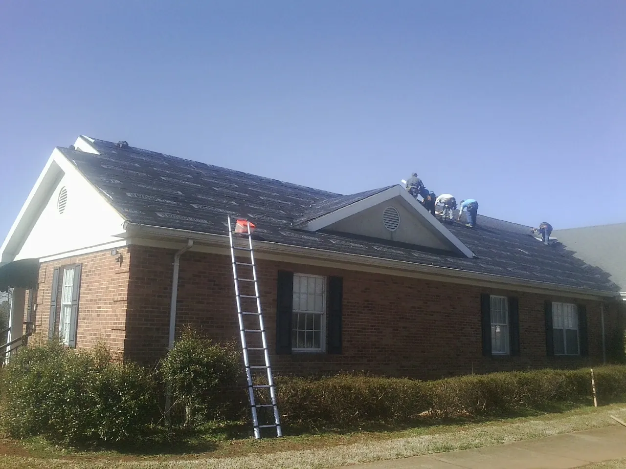 Crew tearing shingles off a brick ranch roof with a ladder set — Emergency Roof Repair work by our crew in Freeman