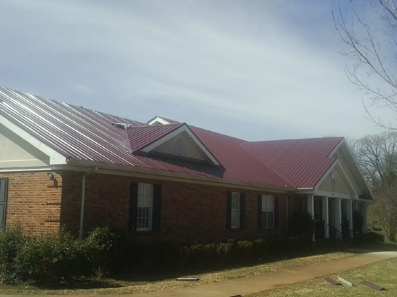 Red metal roof with gabled entries on a long brick building, from a Hail Damage Roof Repair job in Freeman