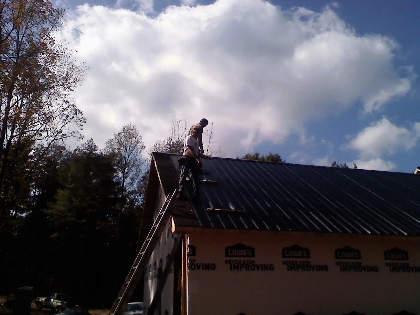 Roofer fastening dark metal panels high against a cloudy sky, from a Roof Inspection job in Freeman