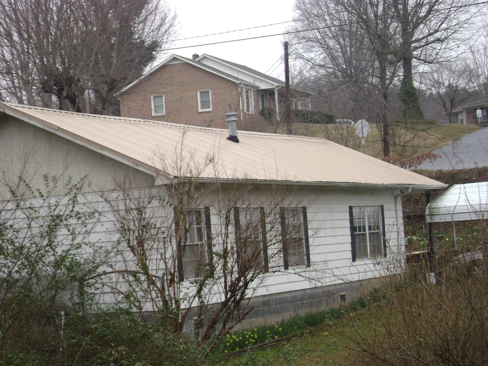 Tan metal roof on a white sided house set into a hillside — Commercial Roofing by Roofing Brothers in Freeman