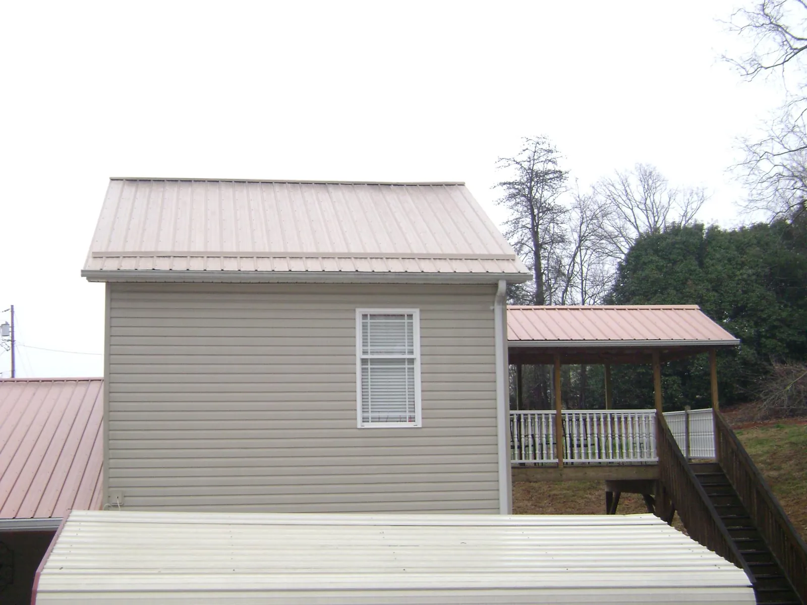 Tan metal roofs on a two story addition and attached porch, from a Roof Replacement job in Freeman